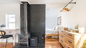 A modern living room with a wood-burning stove, a wooden dresser, a bed, and a desk with a chair. - Charming Ballard Cottage Retreat with Cozy Fireplace (Seattle)