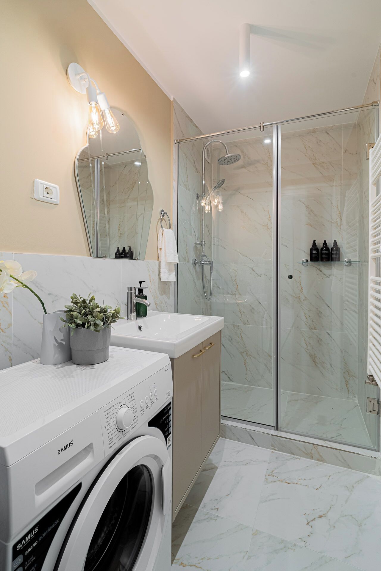 A modern bathroom with a glass-enclosed shower, a built-in washing machine, and a vanity with a mirror.
