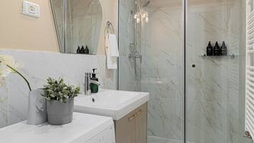 A modern bathroom with a glass-enclosed shower, a built-in washing machine, and a vanity with a mirror.