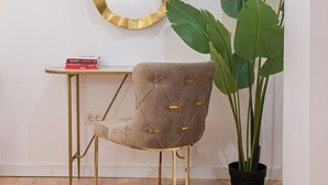 Une pièce comprenant un fauteuil capitonné, un miroir rond avec un cadre doré, une petite table avec des livres et une plante en pot.