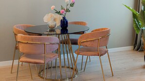 Un coin repas comprenant une table ronde, quatre chaises, un vase avec des fleurs et des luminaires fixés au mur.