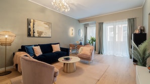 Un salon moderne avec un canapé bleu foncé, un fauteuil rose, une table basse ronde et un lustre.