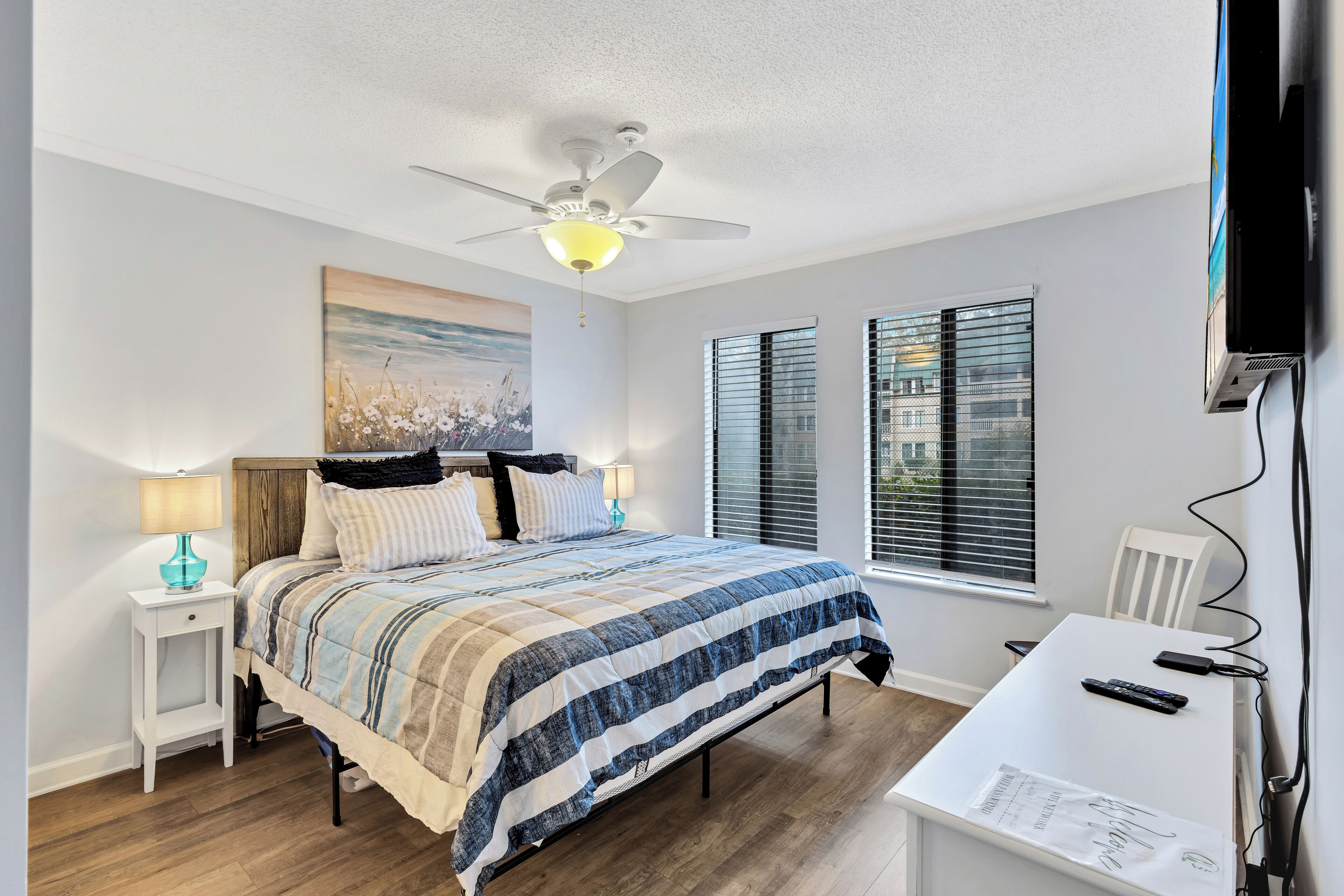 A bedroom with a bed, a desk, a ceiling fan, and a window.