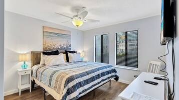 A bedroom with a bed, a desk, a ceiling fan, and a window.