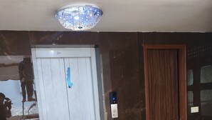 A hotel lobby with a marble floor, a white door with a blue sticker, a wooden door, and a digital display. - Balada Castles Hotel & Resort (Dera Bassi)