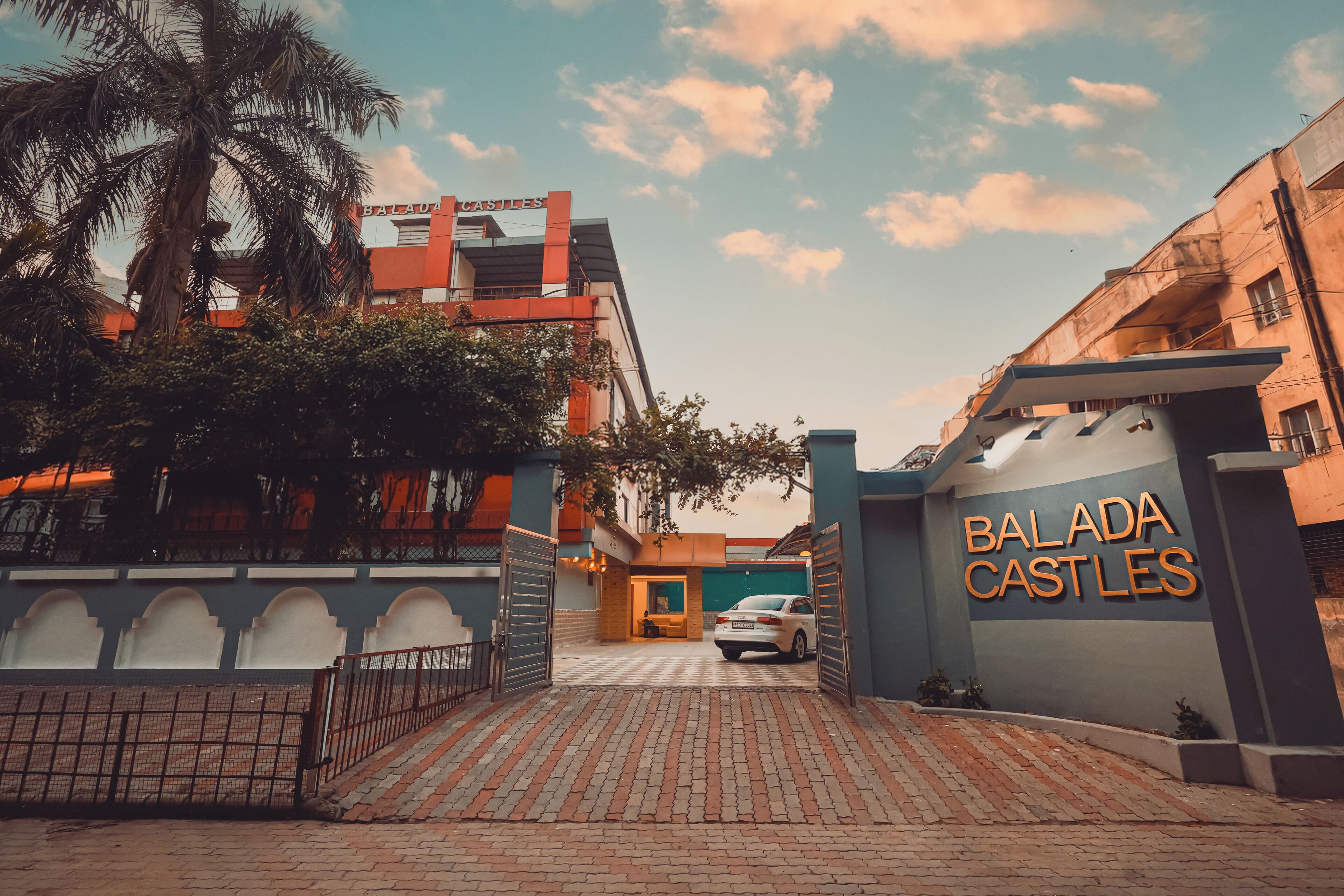 Una entrada con portón a Balada Castles, con un coche estacionado adentro, una palmera y cielo despejado.