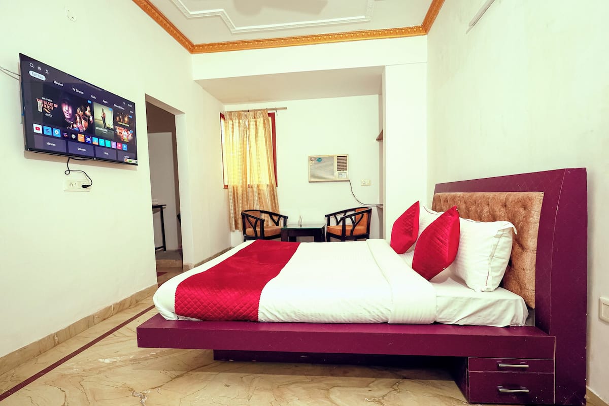 A hotel room with a bed, a TV mounted on the wall, a small table, two chairs, and a window with curtains.
