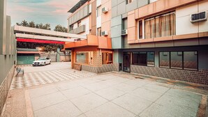 A modern building with a checkered pavement courtyard, a parked car, and a red awning. - Balada Castles Hotel & Resort (Dera Bassi)