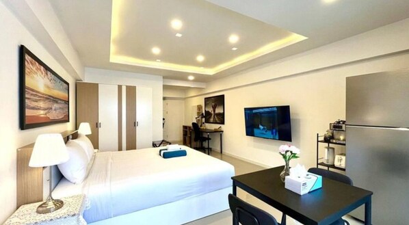A hotel room with a bed, desk, TV, and kitchenette.