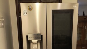 A stainless steel refrigerator with a water dispenser and a freezer compartment, located in a kitchen with tiled flooring and wooden cabinets.