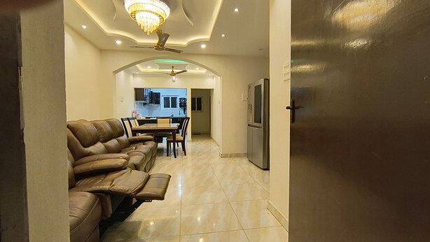 A modern living room with a leather sofa, a dining area with a table and chairs, and a kitchen in the background.