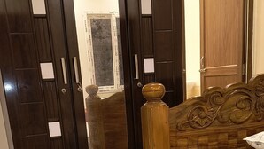 A bedroom with a bed, a wooden headboard, a dark wooden wardrobe with a mirror, and a marble-patterned floor.