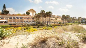 A coastal hotel with multiple balconies, a sandy beach area, and a variety of vegetation. - Studio in Marbella with Beachfront Pool (Marbella)