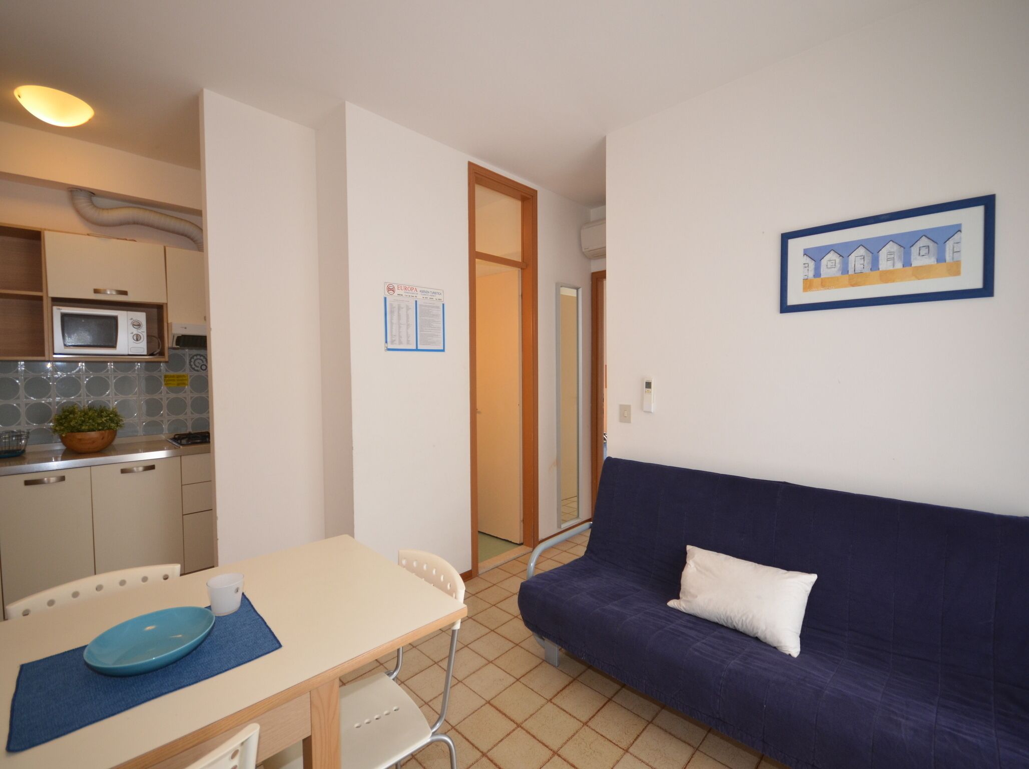 Un espacio habitable compacto con kitchenette, una mesa de comedor con sillas, un sofá y un cuadro en la pared.