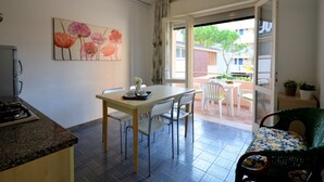 Cocina compacta con comedor, una pequeña mesa y sillas, y vista al balcón exterior.