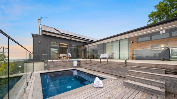 A modern house with a swimming pool, outdoor seating, and large glass windows.
