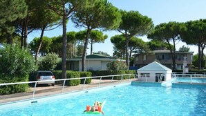 A swimming pool with a lifeguard tower, surrounded by trees and residential buildings. - Spacious apartment with garden - Beahost (Bibione)