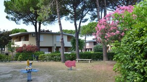 A residential area with apartment buildings, a playground with a swing set, and a pink sculpture. - Spacious apartment with garden - Beahost (Bibione)