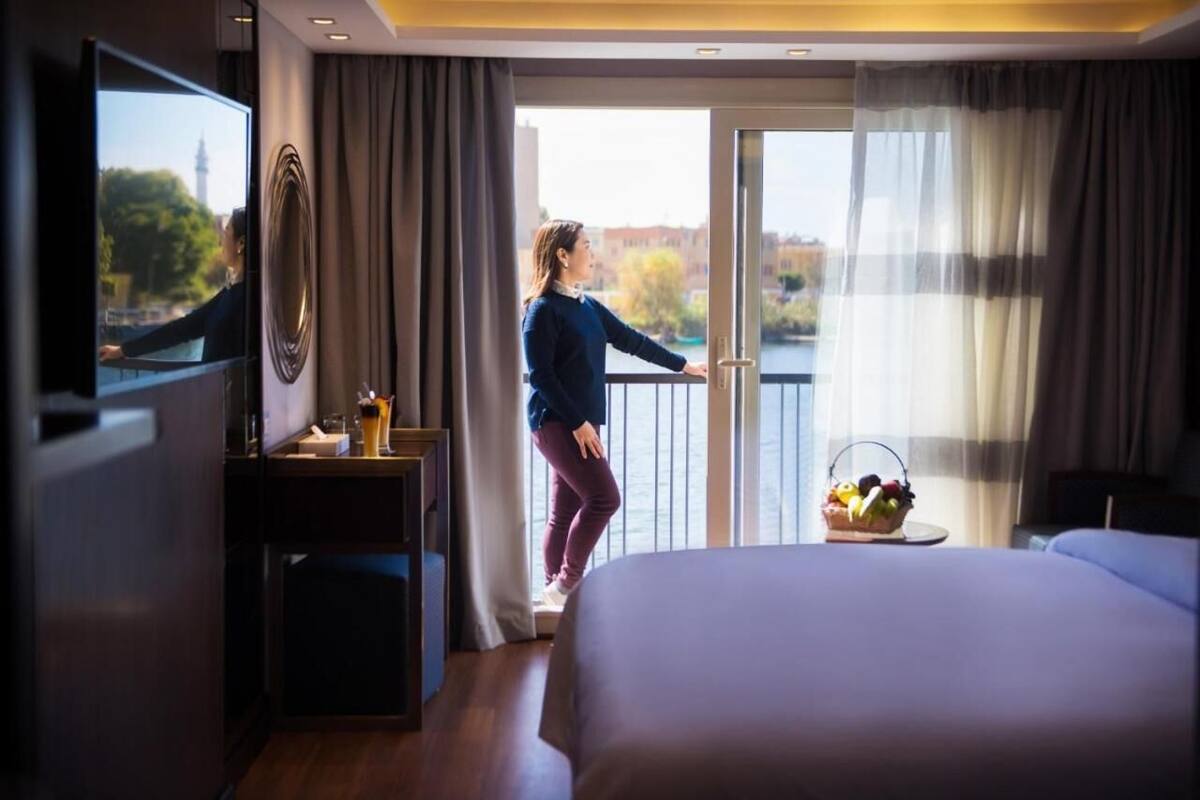 Een hotelkamer met een bed, een televisie, een balkon met uitzicht op een stadsbeeld en een mand fruit op de vensterbank.
