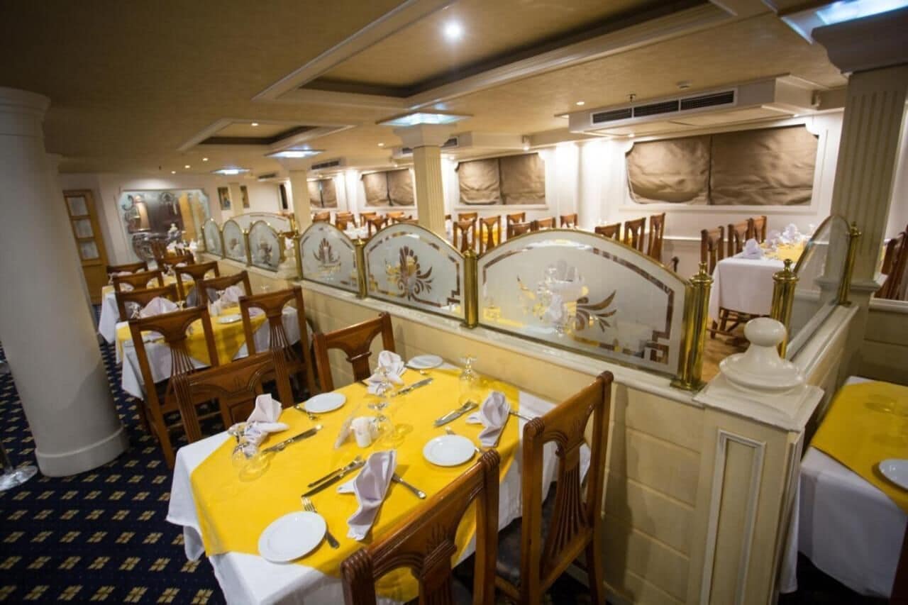 Un elegante comedor con varias mesas dispuestas para el servicio, con adornos ricamente decorados y una decoración clásica.