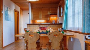 A wooden interior with a dining table and chairs, a kitchen area with a stove and cabinets, and a window with curtains.