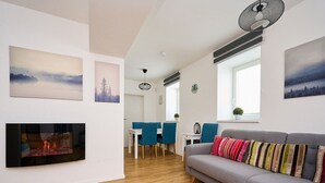 A modern living room with a fireplace, a grey sofa with colorful cushions, a dining area with blue chairs, and artwork on the walls. - Nice apartment for 4 people with WIFI and TV (Jablonec Nad Nisou)