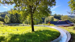 A metal slide in a grassy area with trees and a building in the background. - Nice apartment for 4 people with WIFI and TV (Jablonec Nad Nisou)