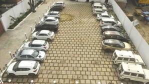 Parcheggio con diverse automobili e alcuni camion, circondato da edifici.