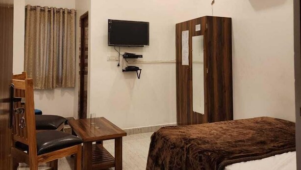 Una camera da letto con un letto, una scrivania in legno, una sedia, una televisione, un armadio e una ventola a soffitto.