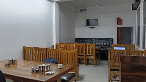 Un'area pranzo con tavoli e sedie in legno, un divano in pelle nera e un televisore montato a parete.