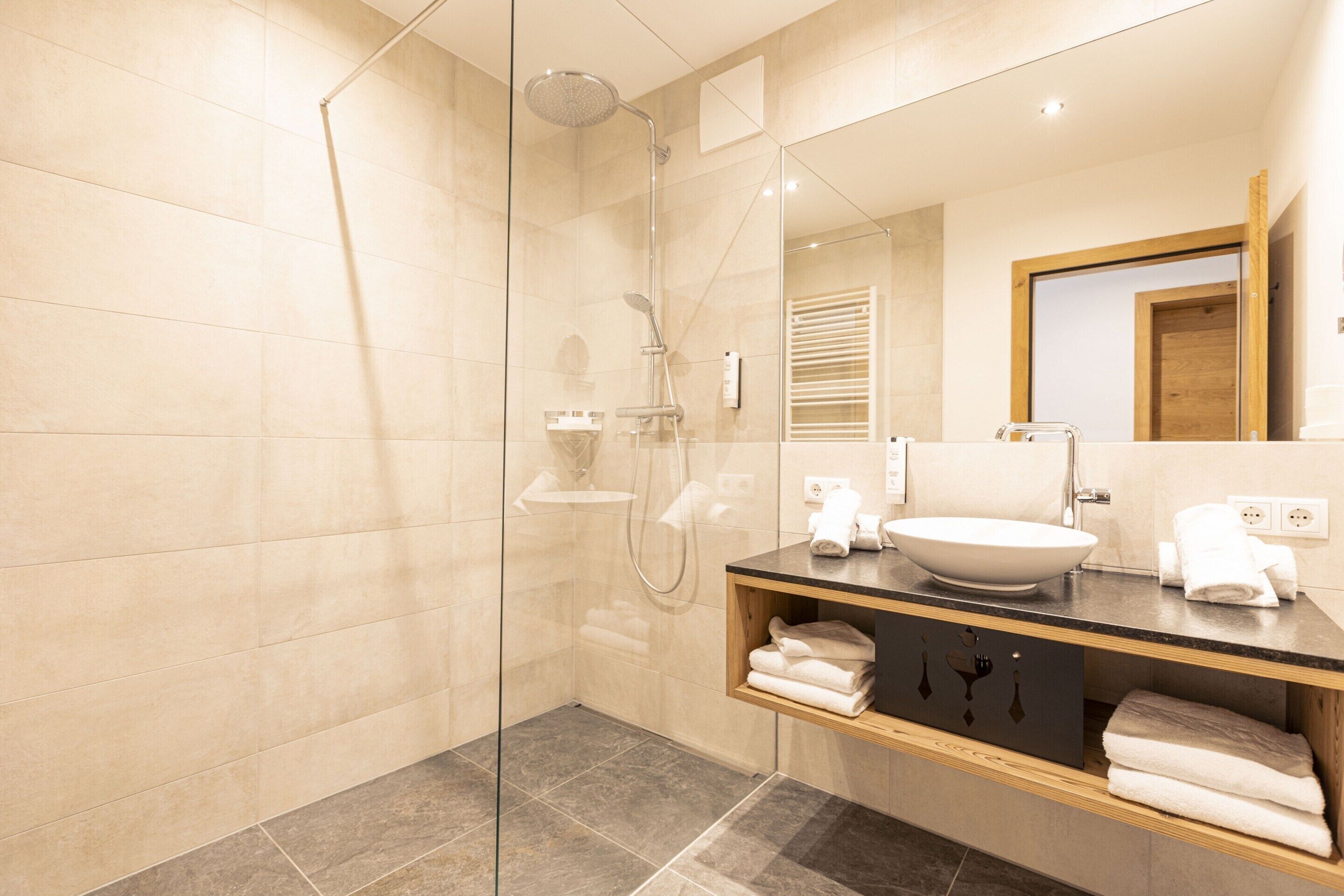 A modern bathroom with a glass-enclosed shower, a sink with a vessel basin, and a wooden vanity with towels.