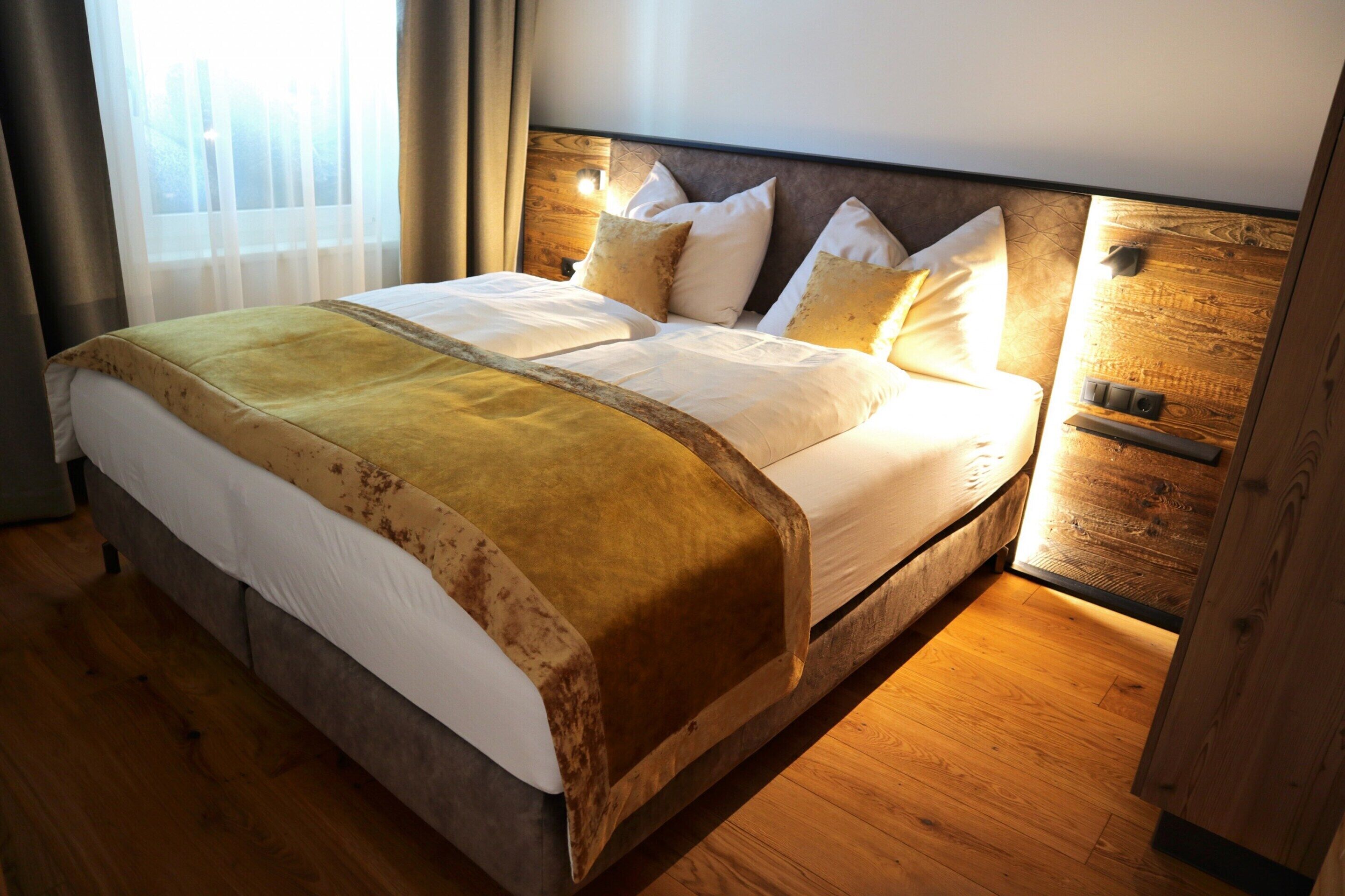Ein großes Bett mit hölzernem Kopfteil, weißen Leinentüchern und einer braunen Tagesdecke.