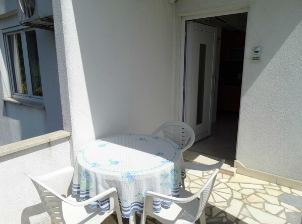 A small outdoor patio with a round table and four chairs, a door leading inside, and a window with blinds.
