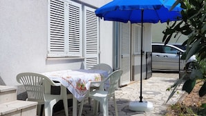 Un patio con una mesa y sillas, una sombrilla azul, y un coche estacionado al fondo.