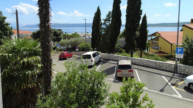 Un estacionamiento con coches, un muro de piedra y vistas al mar y a las montañas.