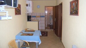 Een kleine keuken met een tafel en stoelen, een klok aan de muur, en een deur naar een badkamer.