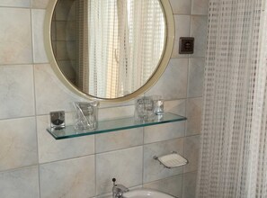 Une salle de bain avec un miroir rond, une étagère en verre où sont rangés les articles de toilette et un porte-serviettes.