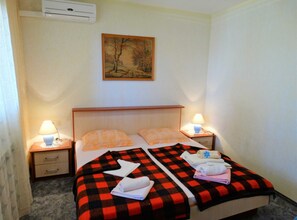 Une chambre d’hôtel comprenant un lit, deux tables de chevet, une commode, un climatiseur et un tableau au mur.