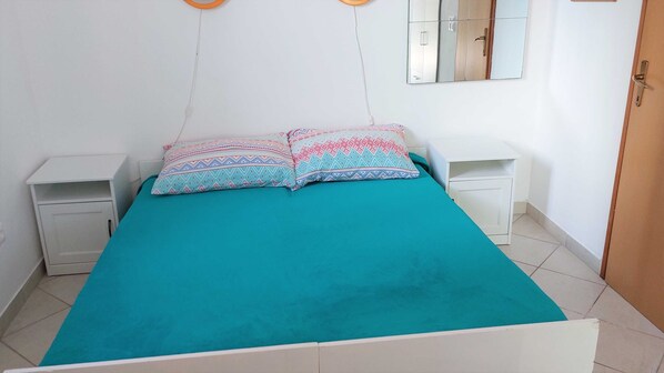 Una cama individual con cubrecama color turquesa y almohadillas estampadas, dos mesitas de noche y un espejo en la pared.