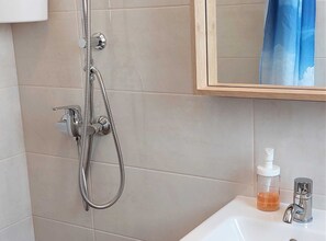 Une salle de bain équipée d’une douche, d’un lavabo, d’un distributeur de savon et d’un miroir.