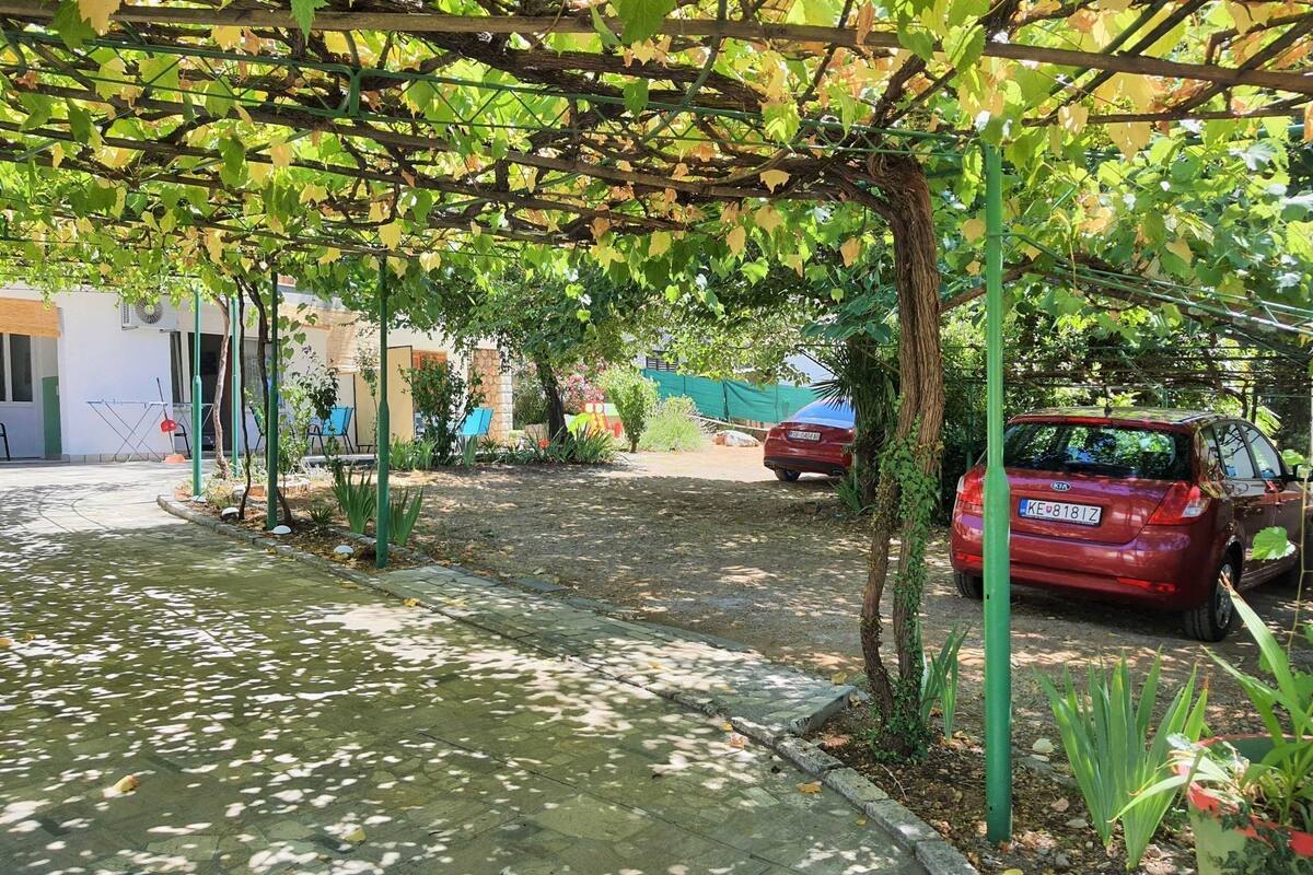 A covered outdoor area with a paved walkway, a red car parked nearby, and a building in the background.