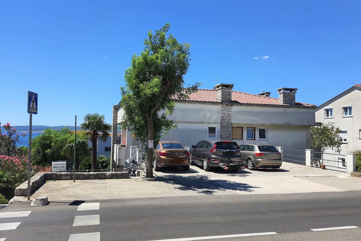 A residential area with a row of parked cars, a pedestrian crossing, and a building with a stone facade.