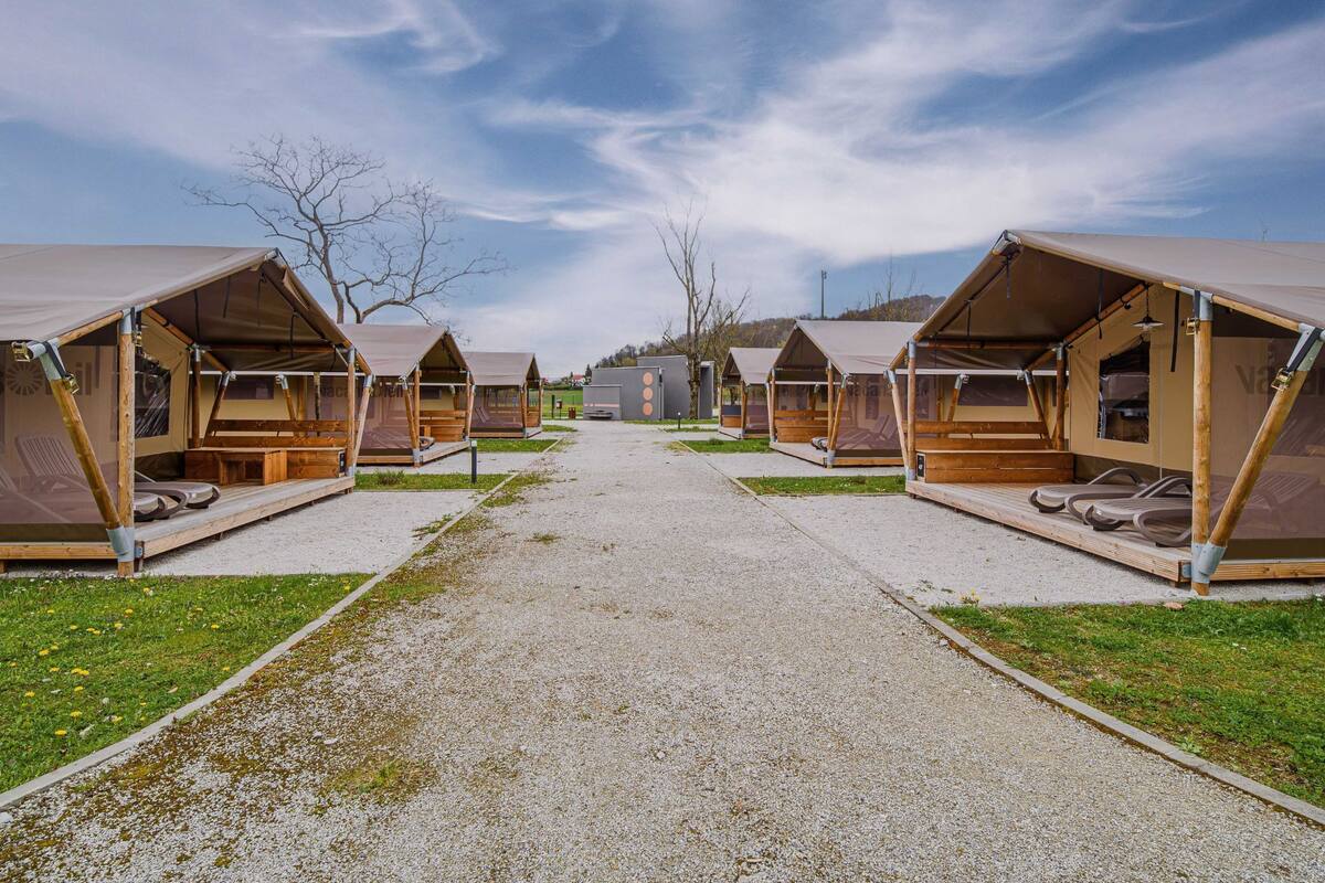 A row of wooden cabins with pitched roofs, arranged along a gravel path with grass on either side.