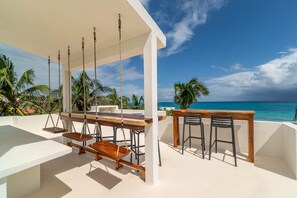 A beachside patio with a swing set, wooden table, and two bar stools. - Ocean View Suite w/pool (Isla Mujeres)