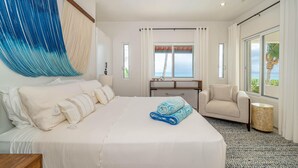 Ein Hotelzimmer mit einem großen Bett, einem Schreibtisch, einem Stuhl und Blick auf den Ozean.