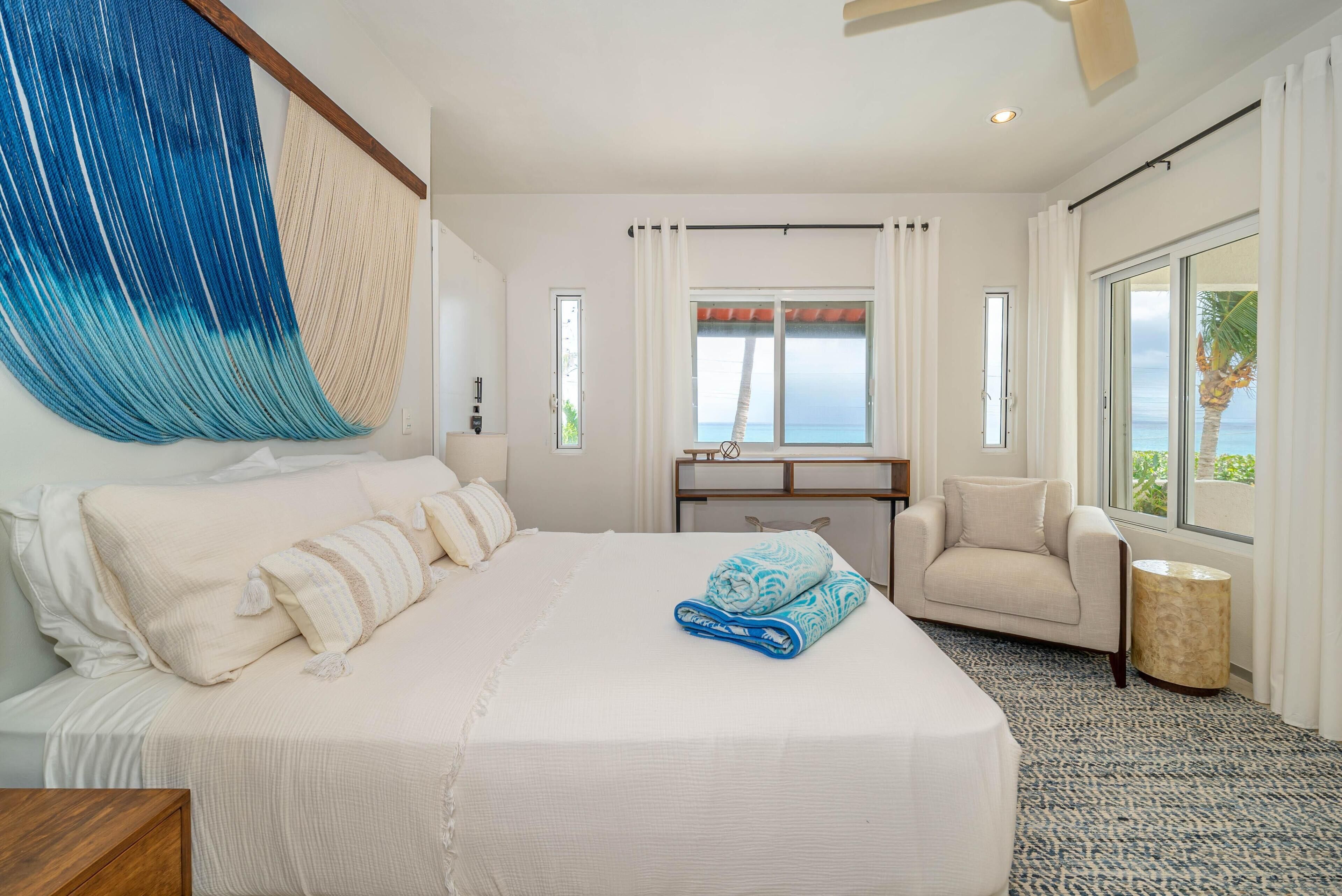 A hotel room with a large bed, a desk, a chair, and a view of the ocean.