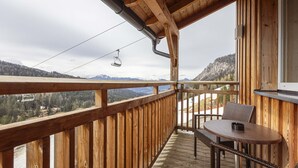 A wooden deck with a table and chairs, overlooking a mountainous landscape and a ski lift.
