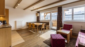 A cozy room with a wooden dining table, chairs, a small sofa, and a window with a view of buildings.