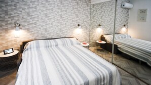 Una habitación de hotel moderna con una cama grande, una mesita de noche con lámpara, una pequeña mesa redonda con una silla y un espejo grande.