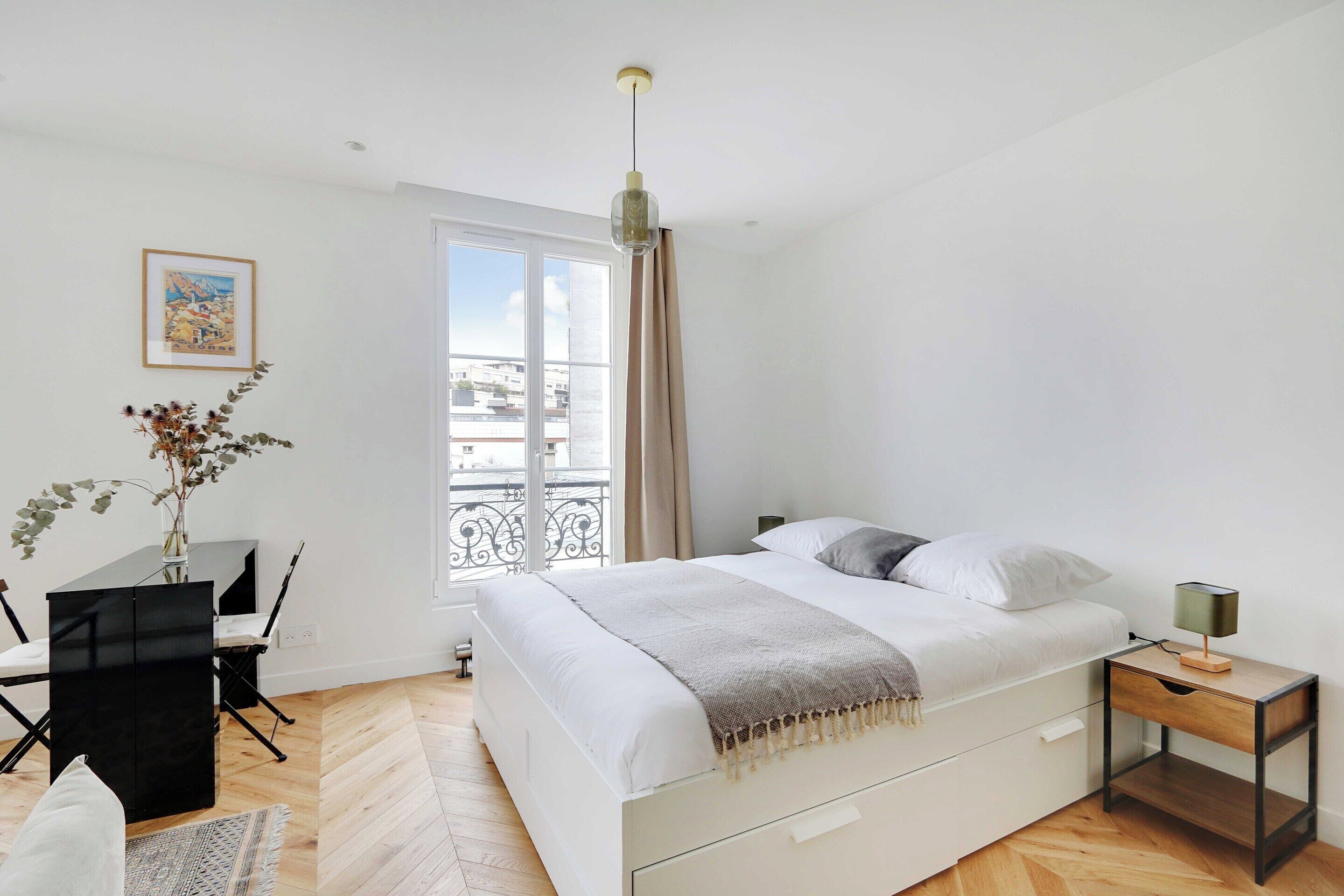 A bedroom with a bed, bedside table, desk, chair, and a window with curtains.